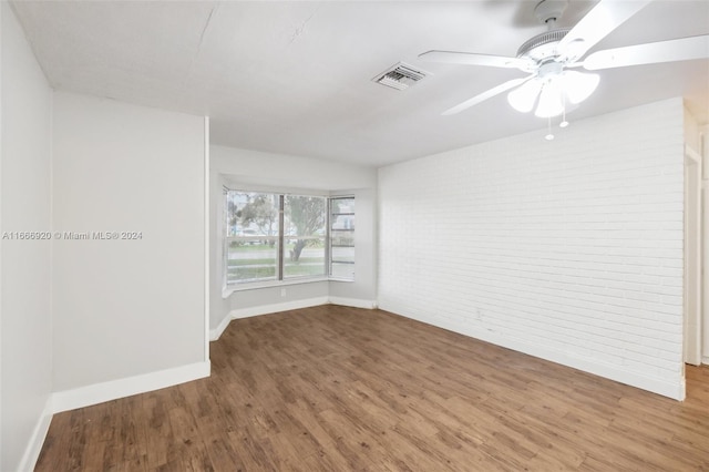 unfurnished room with wood-type flooring, ceiling fan, and brick wall