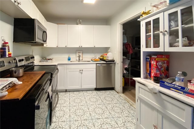 kitchen with light tile patterned floors, appliances with stainless steel finishes, sink, and white cabinetry