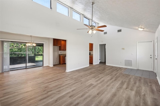 unfurnished living room featuring high vaulted ceiling, light wood-type flooring, a textured ceiling, and ceiling fan with notable chandelier