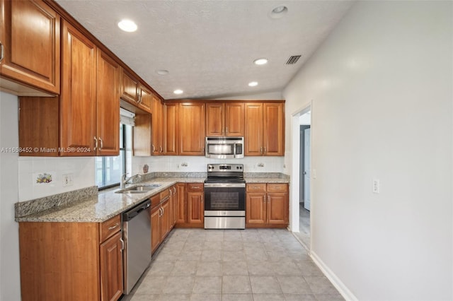 kitchen featuring light stone counters, lofted ceiling, sink, a textured ceiling, and stainless steel appliances