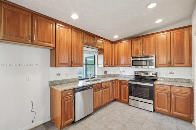 kitchen featuring lofted ceiling, sink, a textured ceiling, appliances with stainless steel finishes, and light stone countertops