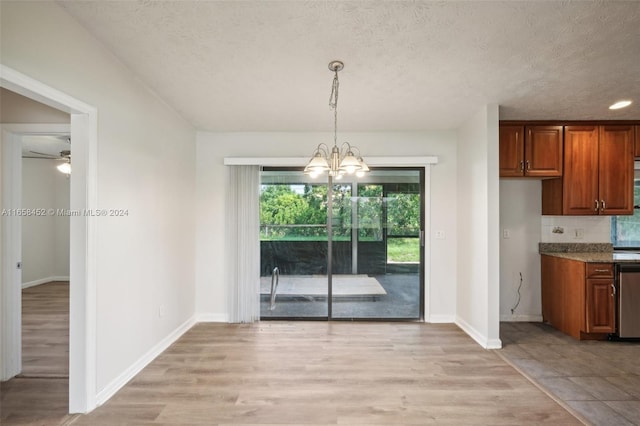 unfurnished dining area with light wood-type flooring, ceiling fan with notable chandelier, and a textured ceiling