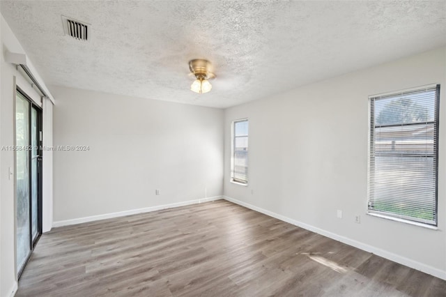 unfurnished room with wood-type flooring, a textured ceiling, and a healthy amount of sunlight