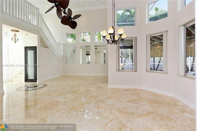 empty room featuring a healthy amount of sunlight, ceiling fan with notable chandelier, crown molding, and a towering ceiling