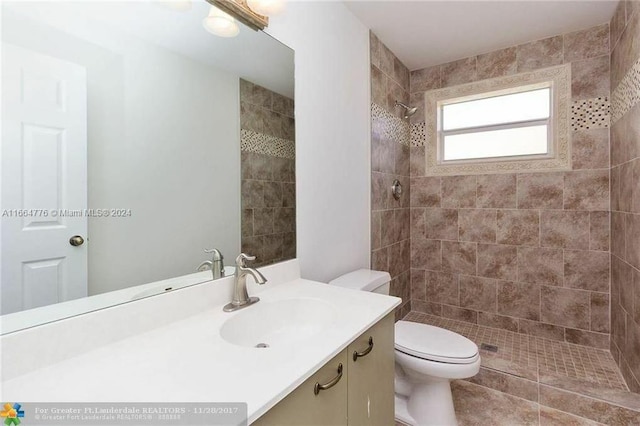 bathroom featuring a tile shower, tile patterned flooring, vanity, and toilet