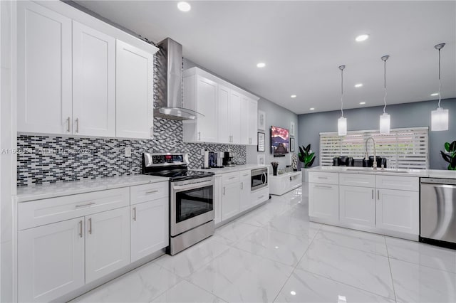 kitchen featuring stainless steel appliances, wall chimney range hood, white cabinetry, pendant lighting, and a sink