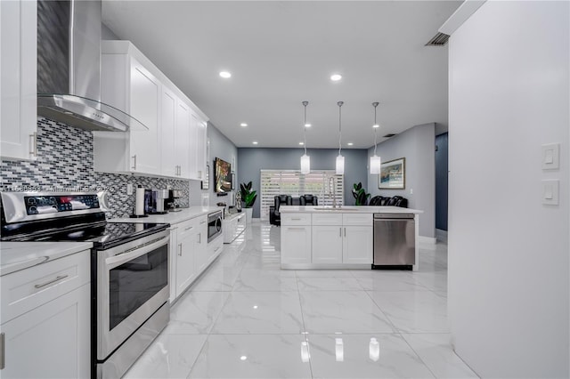 kitchen with tasteful backsplash, white cabinets, wall chimney exhaust hood, appliances with stainless steel finishes, and pendant lighting