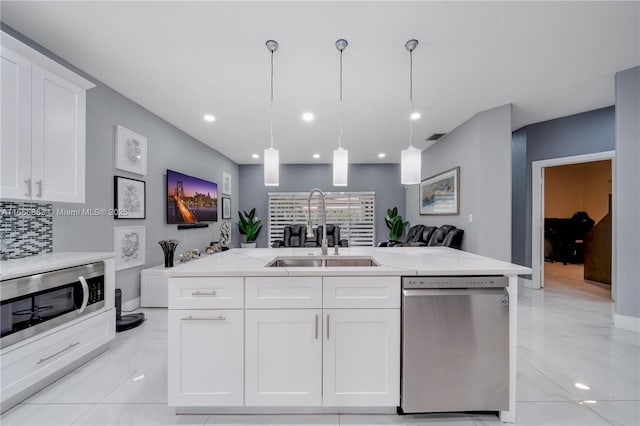 kitchen featuring stainless steel appliances, white cabinets, a sink, and a center island with sink