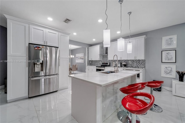 kitchen with appliances with stainless steel finishes, white cabinetry, an island with sink, and a kitchen breakfast bar