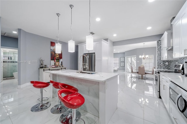 kitchen featuring pendant lighting, a center island with sink, stainless steel appliances, white cabinetry, and a kitchen breakfast bar