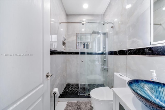 full bathroom with a shower stall, tile walls, toilet, and vanity