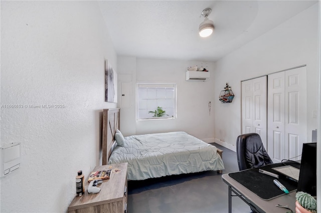 bedroom with a closet, a wall unit AC, finished concrete flooring, and baseboards