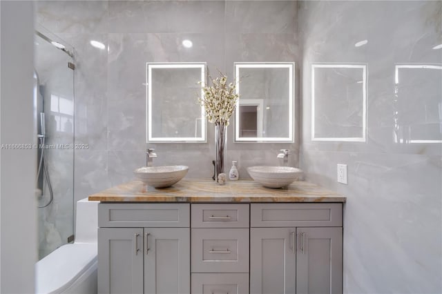 bathroom featuring toilet, double vanity, a sink, and tile walls