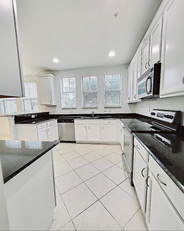 kitchen featuring white cabinets, sink, light tile patterned floors, stainless steel appliances, and dark stone counters