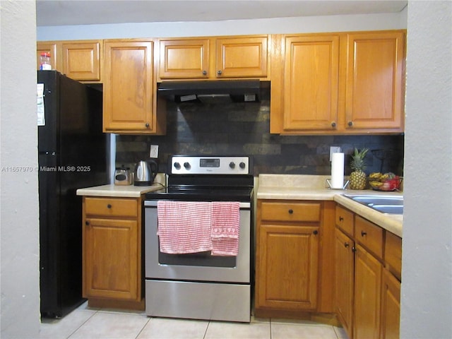 kitchen with electric stove, light tile patterned floors, sink, black refrigerator, and decorative backsplash