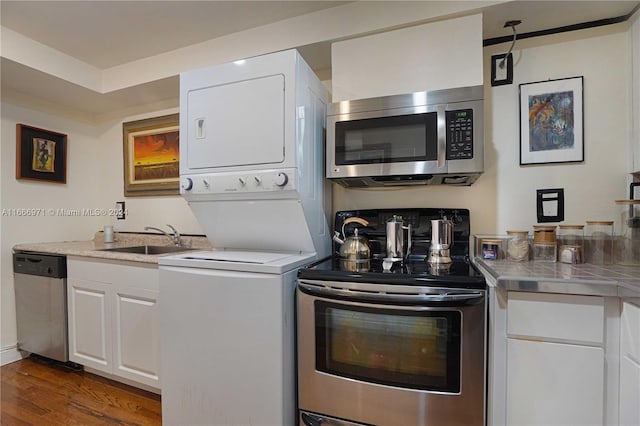 interior space with white cabinets, sink, dark wood-type flooring, stacked washing maching and dryer, and appliances with stainless steel finishes