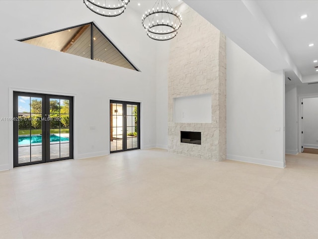 unfurnished living room with french doors, high vaulted ceiling, a chandelier, and a stone fireplace