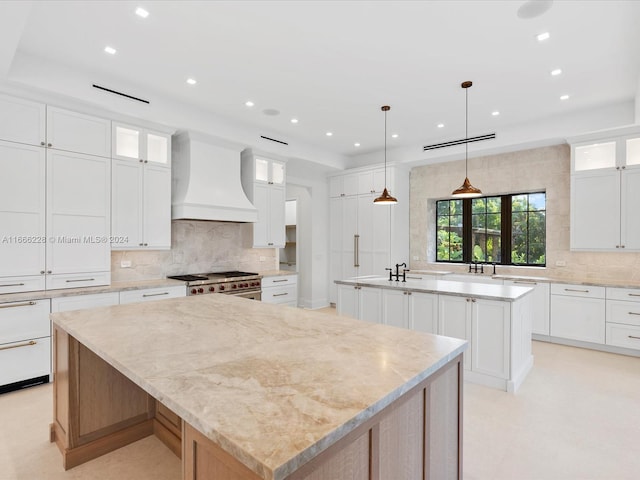 kitchen featuring custom exhaust hood, a large island, high end stainless steel range oven, and white cabinetry