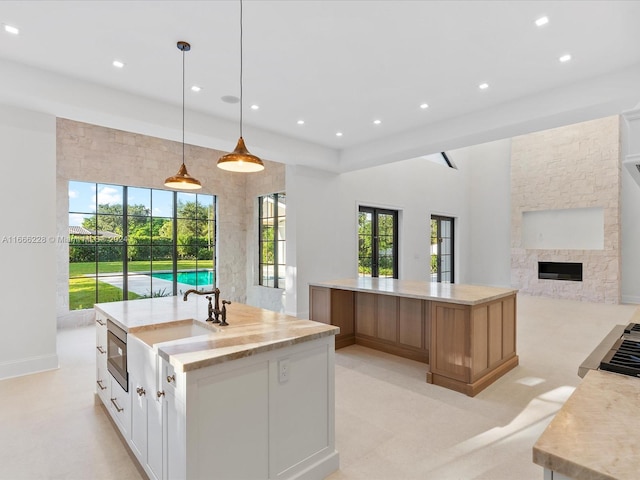 kitchen with sink, a fireplace, hanging light fixtures, white cabinetry, and a large island