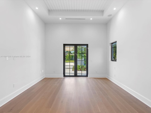 spare room featuring french doors, a tray ceiling, light hardwood / wood-style floors, and a high ceiling