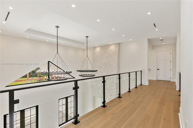 hall with a raised ceiling, a chandelier, and light hardwood / wood-style flooring