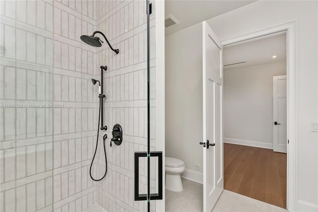 bathroom featuring hardwood / wood-style flooring, tiled shower, and toilet