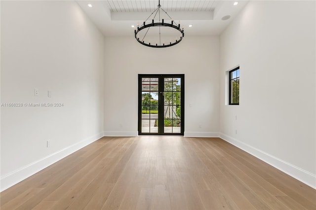 empty room featuring a high ceiling, light wood-type flooring, a notable chandelier, and french doors