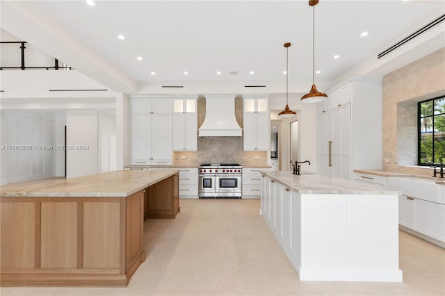 kitchen with a large island with sink, white cabinets, hanging light fixtures, custom exhaust hood, and double oven range