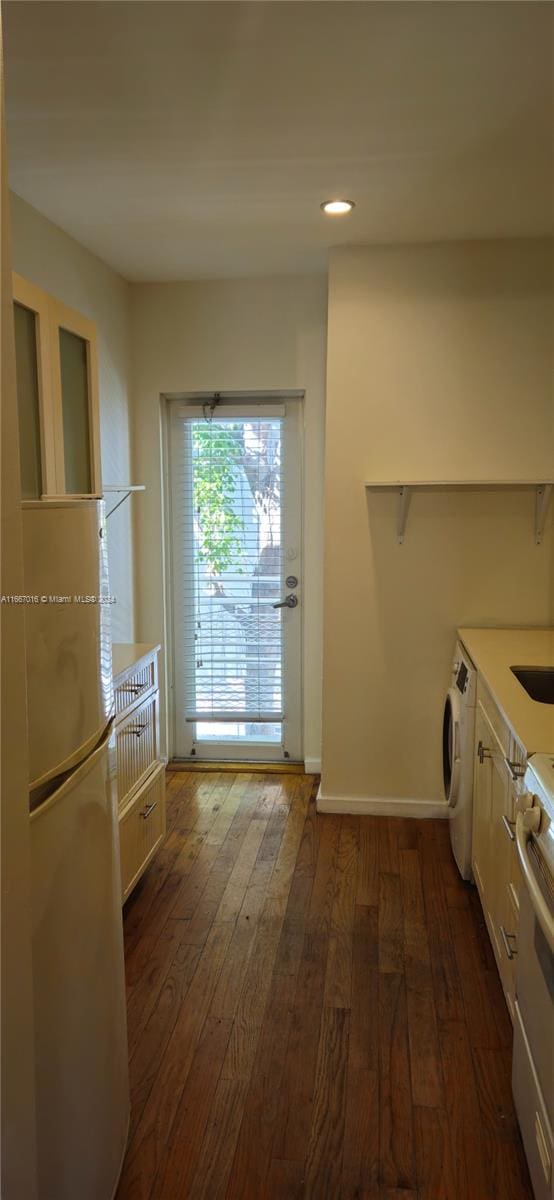 kitchen with dark wood-type flooring, white cabinetry, stainless steel stove, washer / dryer, and white fridge