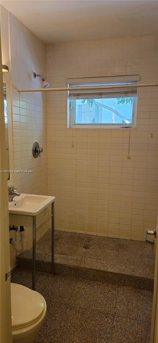 bathroom with a tile shower, tile walls, and toilet