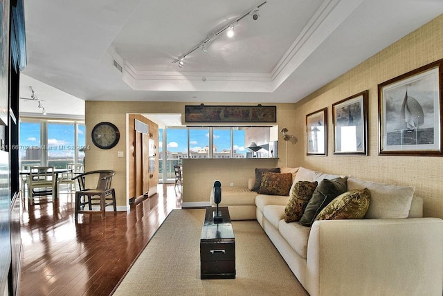 living area featuring crown molding, a raised ceiling, rail lighting, wood-type flooring, and visible vents