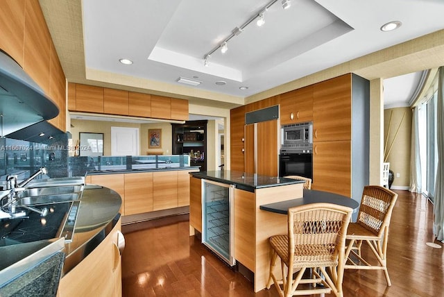 kitchen featuring a raised ceiling, dark countertops, rail lighting, stainless steel microwave, and black oven