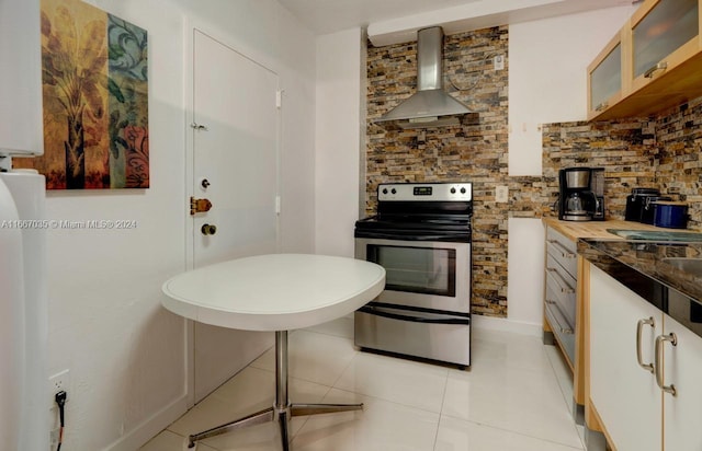 kitchen featuring stainless steel electric range, wooden counters, white cabinetry, wall chimney range hood, and light tile patterned floors