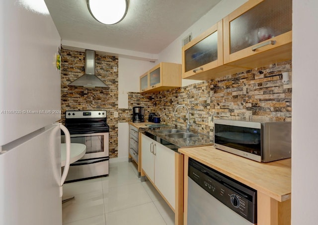 kitchen with sink, appliances with stainless steel finishes, a textured ceiling, light tile patterned floors, and wall chimney range hood