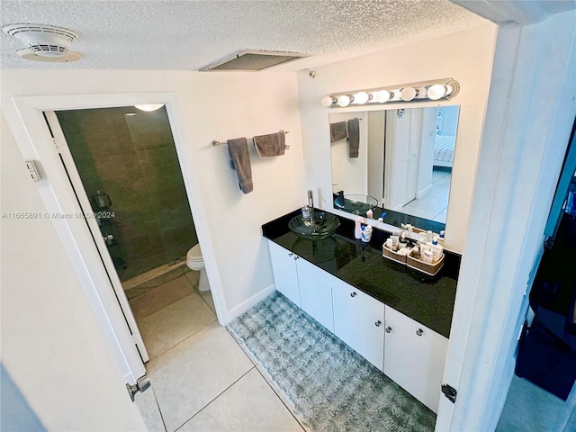 bathroom featuring tile patterned flooring, a textured ceiling, a shower with door, vanity, and toilet