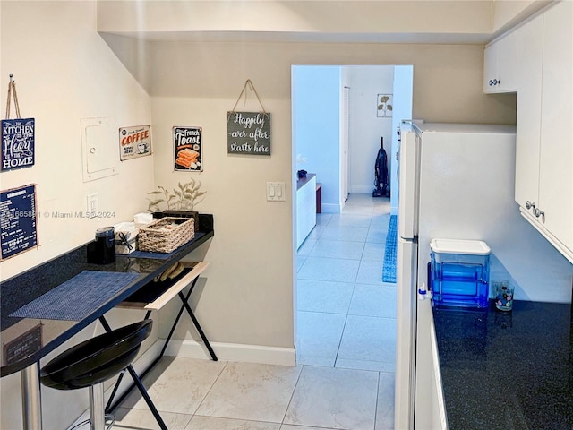 interior space with white refrigerator, light tile patterned floors, and white cabinetry