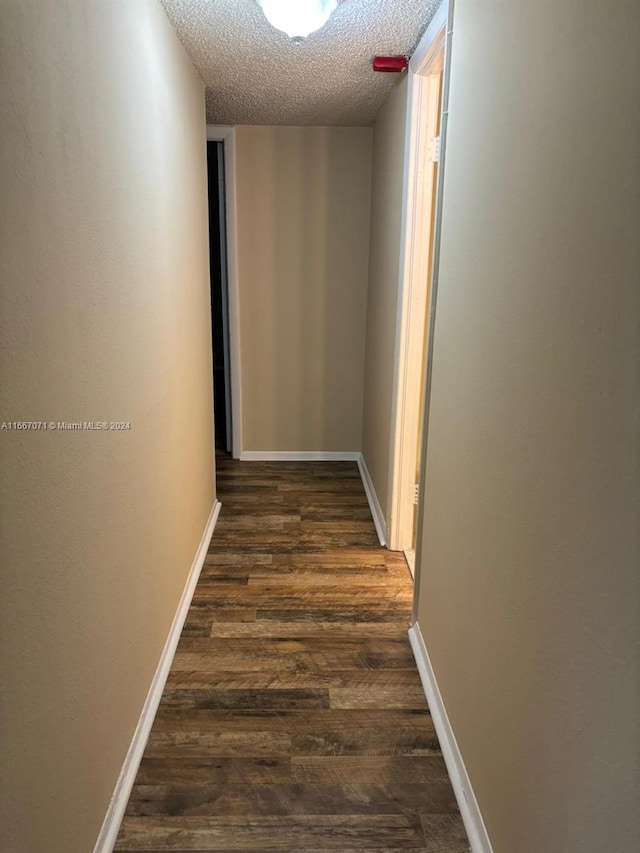 corridor featuring a textured ceiling and dark hardwood / wood-style flooring