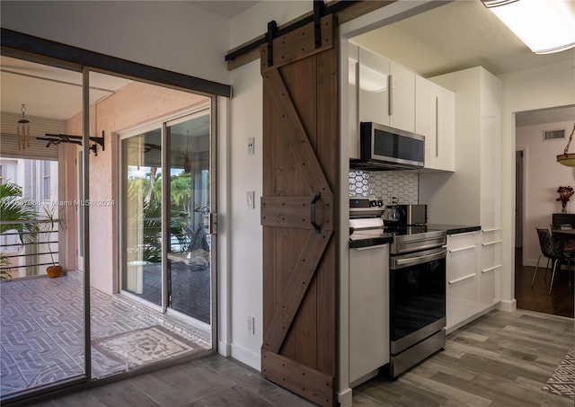 kitchen featuring hardwood / wood-style flooring, white cabinets, a barn door, backsplash, and appliances with stainless steel finishes