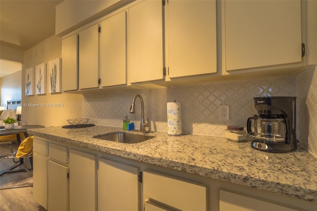 kitchen with decorative backsplash, light hardwood / wood-style floors, sink, and light stone counters