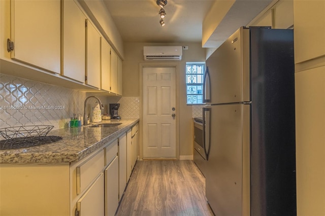 kitchen featuring light hardwood / wood-style floors, a wall unit AC, tasteful backsplash, sink, and appliances with stainless steel finishes