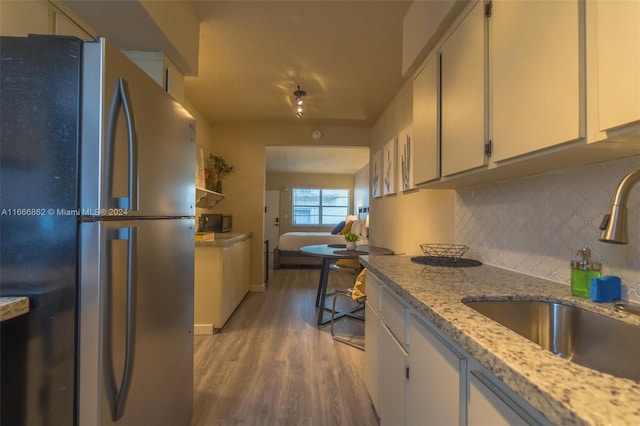 kitchen with tasteful backsplash, stainless steel fridge, hardwood / wood-style flooring, white cabinets, and sink