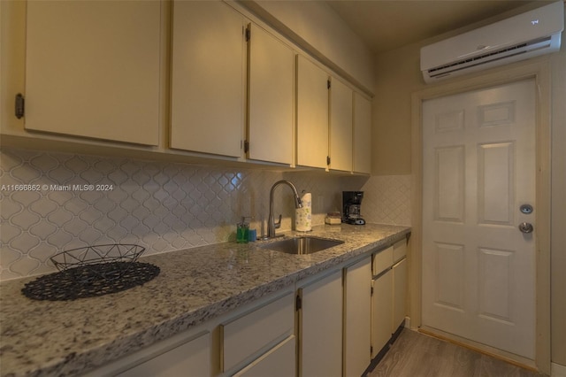 kitchen featuring light wood-type flooring, sink, a wall unit AC, light stone countertops, and decorative backsplash