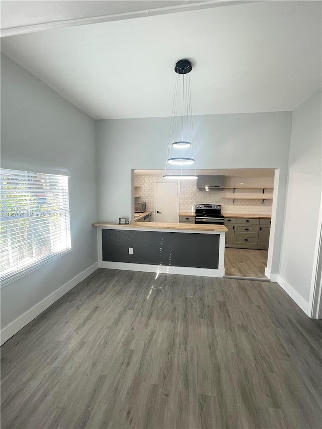 kitchen featuring pendant lighting, stainless steel range oven, dark hardwood / wood-style floors, kitchen peninsula, and wall chimney exhaust hood