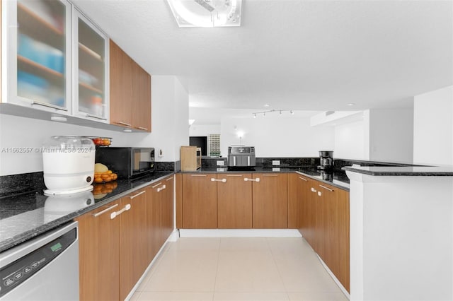 kitchen with dark stone counters, stainless steel dishwasher, light tile patterned floors, and kitchen peninsula