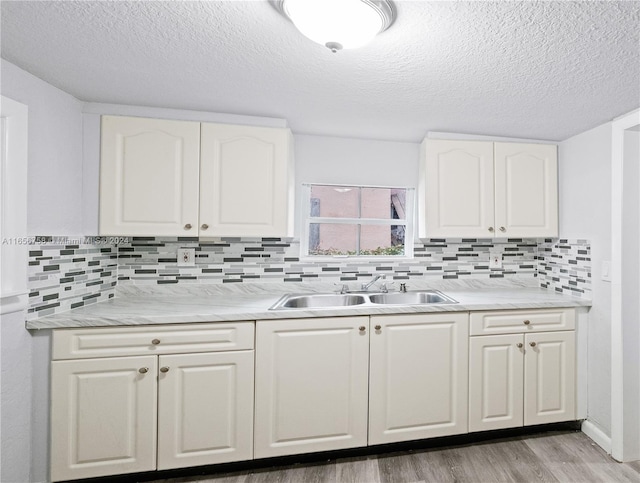 kitchen featuring decorative backsplash, white cabinets, light wood-type flooring, a textured ceiling, and sink