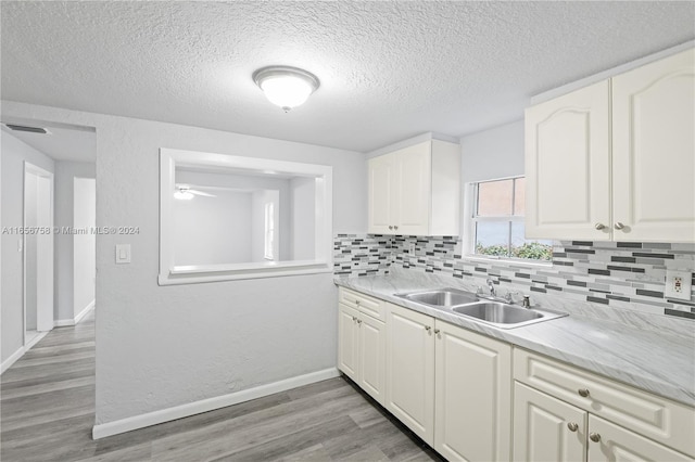 kitchen with light wood-type flooring, backsplash, sink, and white cabinets