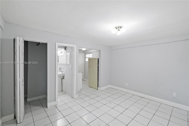 unfurnished bedroom featuring a closet, ensuite bath, light tile patterned floors, and white fridge