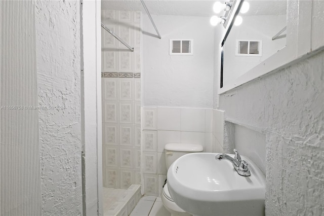 bathroom featuring walk in shower, tile walls, toilet, and sink