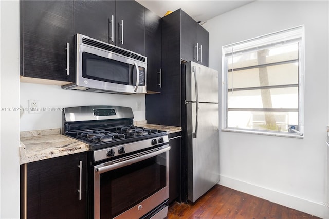 kitchen with appliances with stainless steel finishes, light stone countertops, and dark hardwood / wood-style floors