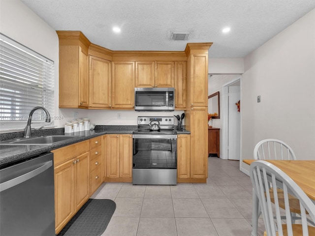 kitchen with light tile patterned floors, sink, a textured ceiling, stainless steel appliances, and dark stone counters